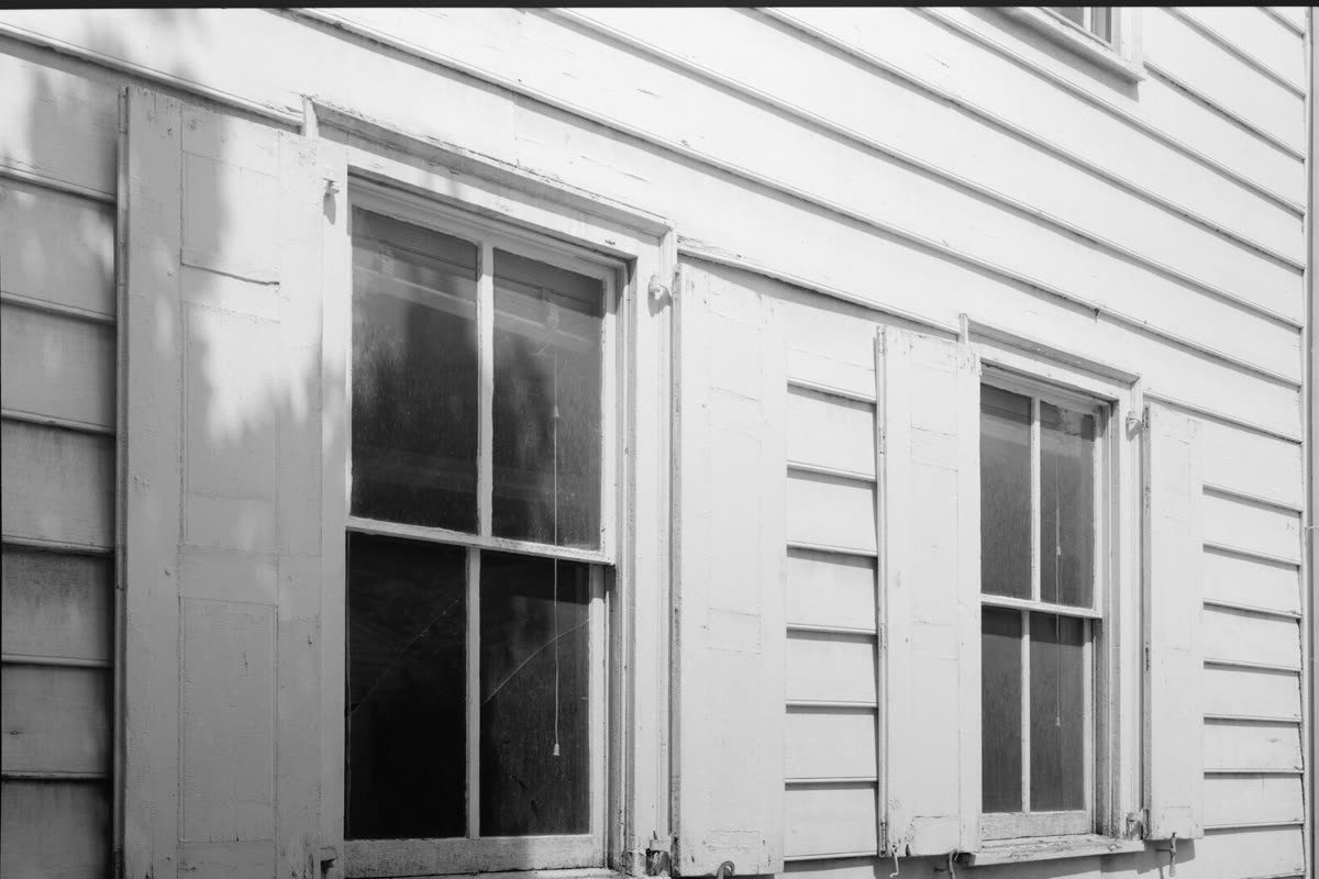 Two sash windows with wooden shutters on the beaded clapboard wall of a house in Kingston, New York